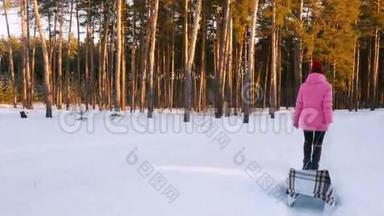 穿着粉红色<strong>羽绒服</strong>的年轻女子在冬天的树林里背着一只空雪橇